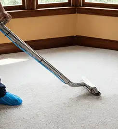 Steam carpet cleaning technician using a hot-water extraction wand on a residential carpet, wearing blue protective shoe covers Cleveland, OH.