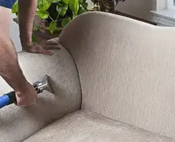 Professional upholstery cleaner deep-cleaning a fabric sofa with a handheld extraction tool and hose in Cleveland, OH.